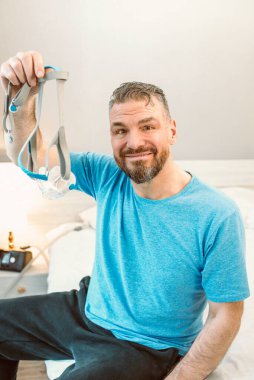 Kronik solunum sorunu olan olgun, mutlu bir adam yatak odasında CPAP makinesiyle yatmayı düşünüyor. Sağlık, CPAP, horlama konsepti