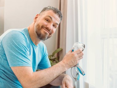 Kronik solunum sorunu olan olgun, mutlu bir adam yatak odasında CPAP makinesiyle yatmayı düşünüyor. Sağlık, CPAP, horlama konsepti