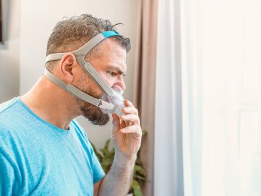 Mutsuz, şok olmuş, kronik solunum sorunu olan bir adam yatak odasında CPAP makinesini kullanarak şaşırdı. Sağlık, CPAP, uyku apnesi terapisi, horlama konsepti