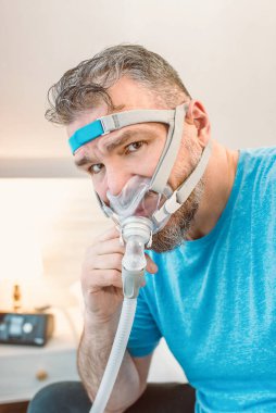 Mutsuz, şok olmuş, kronik solunum sorunu olan bir adam yatak odasında CPAP makinesini kullanarak şaşırdı. Sağlık, CPAP, uyku apnesi terapisi, horlama konsepti