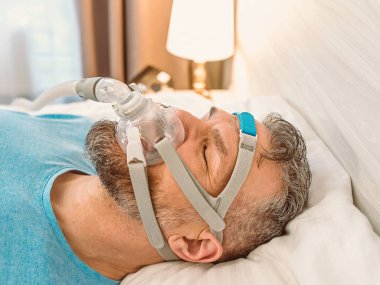 Kronik solunum sorunu olan uyuyan adam yatakta CPAP makinası kullanmayı düşünüyor. Sağlık, obstrüktif uyku apnesi terapisi, CPAP, horlama konsepti