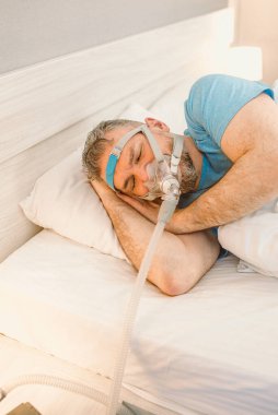 Kronik solunum sorunu olan uyuyan adam yatakta CPAP makinası kullanmayı düşünüyor. Sağlık, obstrüktif uyku apnesi terapisi, CPAP, horlama konsepti