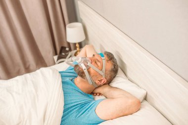 Kronik solunum sorunu olan uyuyan adam yatakta CPAP makinası kullanmayı düşünüyor. Sağlık, obstrüktif uyku apnesi terapisi, CPAP, horlama konsepti
