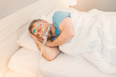 Kronik solunum sorunu olan uyuyan adam yatakta CPAP makinası kullanmayı düşünüyor. Sağlık, obstrüktif uyku apnesi terapisi, CPAP, horlama konsepti