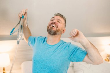 Yatak odasındaki yatakta oturan CPAP makinesini kullandıktan sonra kronik solunum problemi olan mutlu dinlenmiş bir adam. Sağlık, CPAP, uyku apnesi terapisi, horlama konsepti