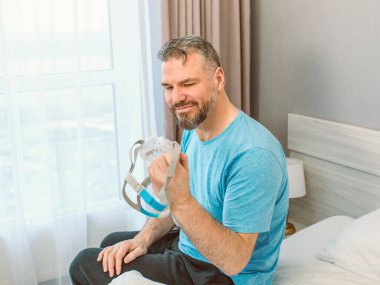 Kronik solunum sorunu olan olgun, mutlu bir adam yatak odasında CPAP makinesiyle yatmayı düşünüyor. Sağlık, CPAP, horlama konsepti