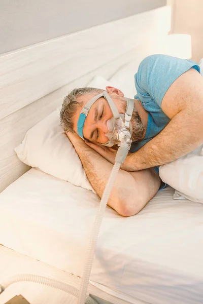 Sleeping man with chronic breathing issues considers using CPAP machine in bed. Healthcare, Obstructive sleep apnea therapy, CPAP, snoring concept