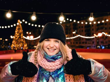 Buz pistinde şapkalı, atkılı ve eldivenli gülümseyen genç bir kadın. Aktif yaşam tarzı, buz pateni, kış sporları