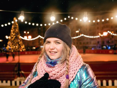 Buz pistinde şapkalı, atkılı ve eldivenli gülümseyen genç bir kadın. Aktif yaşam tarzı, buz pateni, kış sporları