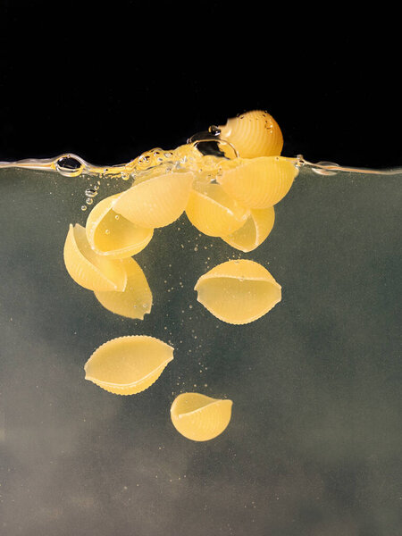 seashell pasta falling in the boiling water on dark background. Underwater view. Cooking, cooking at home, italian cuisine concept