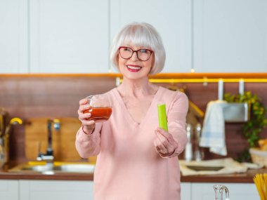 Mutfakta diyette kereviz ve domates suyu ile kıdemli neşeli kadın. Çiğ, vejetaryen, diyet, mutfak konsepti