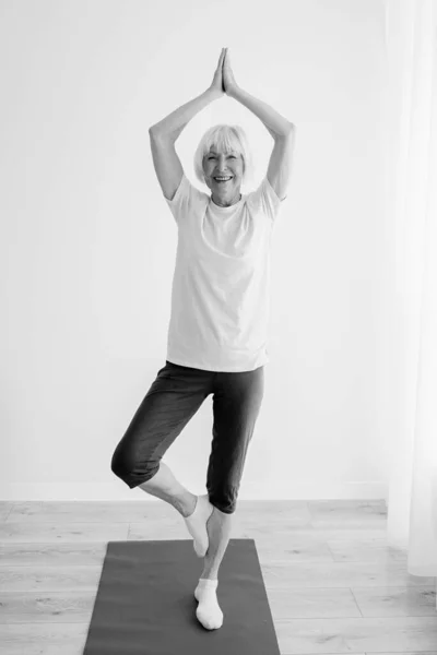 monochrome portrait of senior woman doing yoga home indoor. Anti age, sport, yoga concept