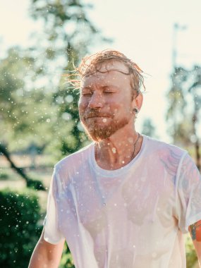 Kafkasyalı bir adamın su sıçramalarıyla kafasını salladığı portre. Yaz eğlencesi, parti, tatil, duygular, zevk, rahatlama, ferahlatıcı konsept