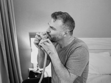 Yatak odasındaki yatakta oturan CPAP makinesini kullandıktan sonra kronik solunum sorunu olan Happy 'nin monokrom portresi. Sağlık, CPAP, uyku apnesi terapisi, horlama konsepti