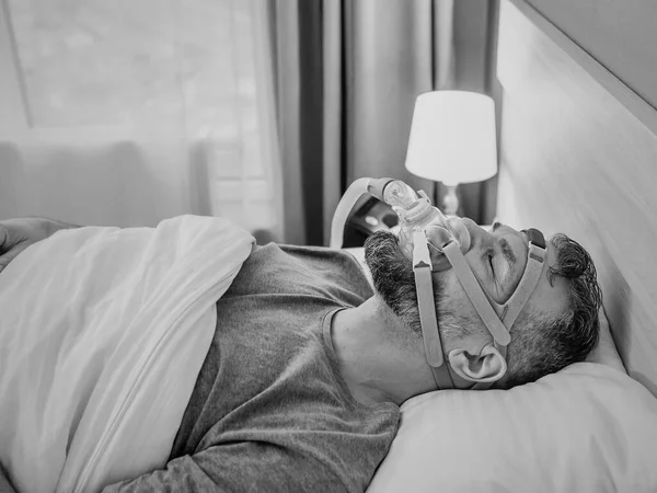 stock image Monochrome portrait of Sleeping man with chronic breathing issues considers using CPAP machine in bed. Healthcare, Obstructive sleep apnea therapy, CPAP, snoring concept