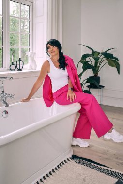 Güzel, şık, kendine güvenen esmer modern iç kısımda banyo modaya uygun fuşya takım elbise içinde. Moda, ev, seyahat, otel konsepti