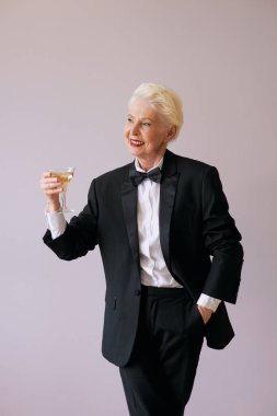 Şık, olgun şarap garsonu smokinli, köpüklü şaraplı yaşlı kadın. Eğlence, parti, tarz, yaşam tarzı, alkol, kutlama konsepti