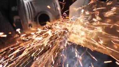 Bir adam dairesel testere ile çalışıyor. Sıcak metalden kıvılcımlar çıkıyor. Yavaş çekim. Yakın çekim.