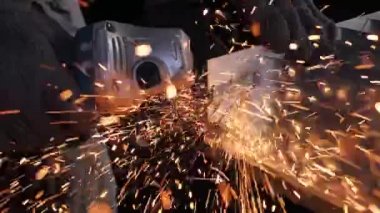 Bir adam dairesel testere ile çalışıyor. Sıcak metalden kıvılcımlar çıkıyor. Yavaş çekim. Yakın çekim.