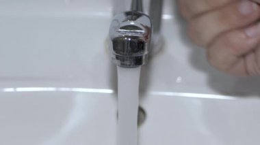 Bir adam ellerini musluğun altında yıkıyor.