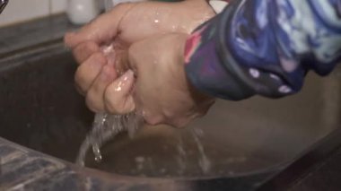 Bir adam ellerini musluğun altında yıkıyor.