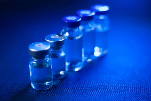 Yanında aşı olan cam bir ilaç şişesi var. Mavi ışık tepede parlıyor. Şişeler bulanık.