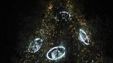Geceleyin ışıklarla süslenmiş Noel ağacı. Kar, büyük kar taneleriyle yağıyor.