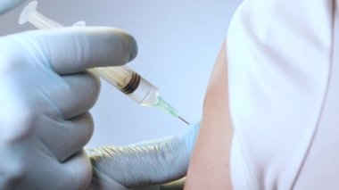 Doktor bir insanın omzuna iğne yapar. Omzuna yakın çekim yapılan bir şırınga. Hastalığa karşı aşı.
