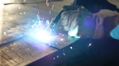 Masadaki kaynakçı bir takım metal parçaları kaynaklıyor. Kaynakçı çalışıyor. Metalle çalışmak