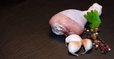 Siyah arka planda yeşillikler olan taze tavuk budu.