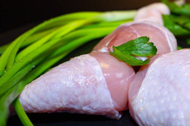 Siyah arka planda yeşillikler olan taze tavuk budu.