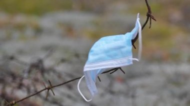 Tıbbi tek kullanımlık mavi koruyucu maske, dikenli tellerde, Coronavirus Covid-19 virüs atığında rüzgarda savruluyor. Çöp toplama. Yeşil gezegen Dünya