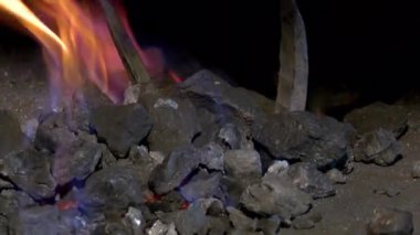 Yangında demirci, metali ısıtarak bir ürün oluşturur. Fırında kırmızı kömür var.