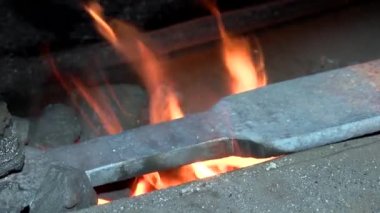 Yangında demirci, metali ısıtarak bir ürün oluşturur. Fırında kırmızı kömür var.