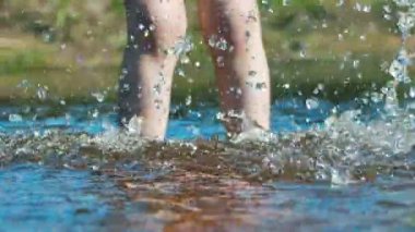 Çıplak ayaklı bir çocuk nehir kıyısında duruyor. Ellerinle her tarafına su püskürt.