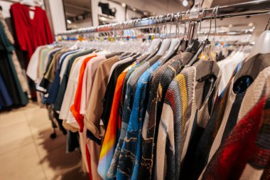 Canlı bir alışveriş deneyimi için temiz plastik askılara yerleştirilmiş, bir giyim mağazasında sergilenen renkli üst ve elbise seçimleri.