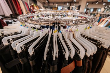 Bir moda mağazasında plastik askıların üzerinde düzgünce düzenlenmiş dairesel giysi rafı, çeşitli boyutlarda ve tarzlarda pantolonları iyi organize edilmiş bir perakende vitrininde sergiliyor..