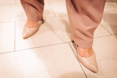 Yumuşak pembe tonlarda, bereli, inci takılı ve ombr eşarplı şık bir kadın zarif giyim rafları arasında bir moda mağazasında güven içinde poz veriyor. 06.10. 2025 Valmiera, Letonya