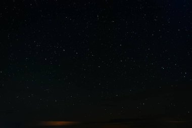 Gökyüzü sayısız yıldızla dolu açık bir gece uzak bir arazinin üzerinde sönük şehir ışıkları ve sıcak bir ufukta parlayan bulutlarla..