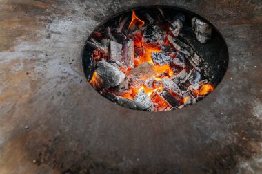 Yuvarlak bir ateş çukurundan yükselen alevler, üzerinde metal bir pişirme halkası olan, sakin, kırsal bir sonbahar ortamında, sakin bir göletin yanına kurulmuş..