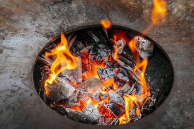 Yuvarlak bir ateş çukurundan yükselen alevler, üzerinde metal bir pişirme halkası olan, sakin, kırsal bir sonbahar ortamında, sakin bir göletin yanına kurulmuş..