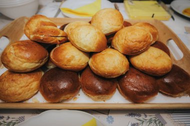 Ahşap tepsilerde dizilmiş çoklu altın sarısı ekmek rulolarının yakın çekim görüntüsü. Yeni pişmiş ve mutfak tezgahında servis için hazır..