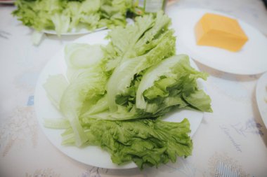 Kıtır yeşil marul yaprakları ve ince soğan dilimleri arkaplanda çedar peyniri dilimleri ile beyaz bir tabakta sıralanmış..