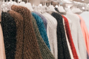 Perakende satış ortamında sergilenen canlı örülmüş süveter koleksiyonu, çeşitli doku ve renkleri vurguluyor, kışın moda tutkunları için ideal