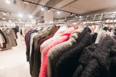 Çağdaş bir mağazada giysi rafında sergilenen süveterler, çeşitli renk ve dokulara sahip, moda tutkunları için canlı bir alışveriş ortamı yaratıyor.