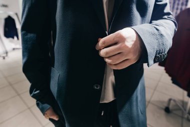 Adam modern bir giyim mağazasında koyu renk ceketin düğmesini ayarlıyor. Moda detaylarını ve modern perakende satış atmosferini vurguluyor.