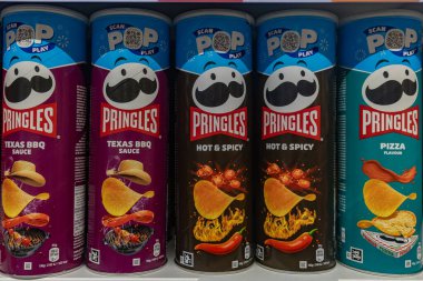 Valmier, Letonya - 24 Kasım 2025: Pringles abur cubur kutuları Texas BBQ, Hot & Spicy ve Pizza aromalarını renkli markalar ve ürün çeşitliliğini vurguluyor