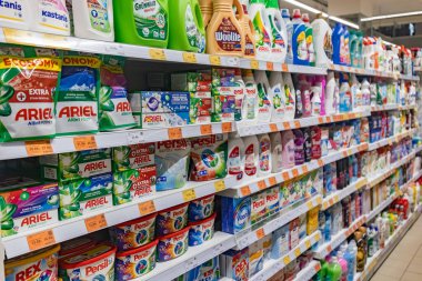 Valmier, Letonya - 24 Kasım 2025: Süpermarkette renkli ambalaj ve marka isimlerine sahip çok çeşitli çamaşır deterjanı ve temizlik ürünleri sergileniyor