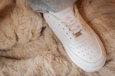 Valmier, Letonya - 24 Kasım 2025: Beyaz spor ayakkabılar yumuşak, sahte bir kürk battaniyeye konur ve rahat bir atmosferde çağdaş tarz ve konforu vurgular.