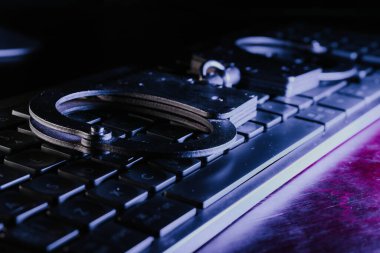 Suç ve adalet temalarını temsil eden bir klavyeye yerleştirilmiş kelepçeler, kolluk kuvvetlerinin ve dijital güvenliğin havasını artıran karanlık bir zemin